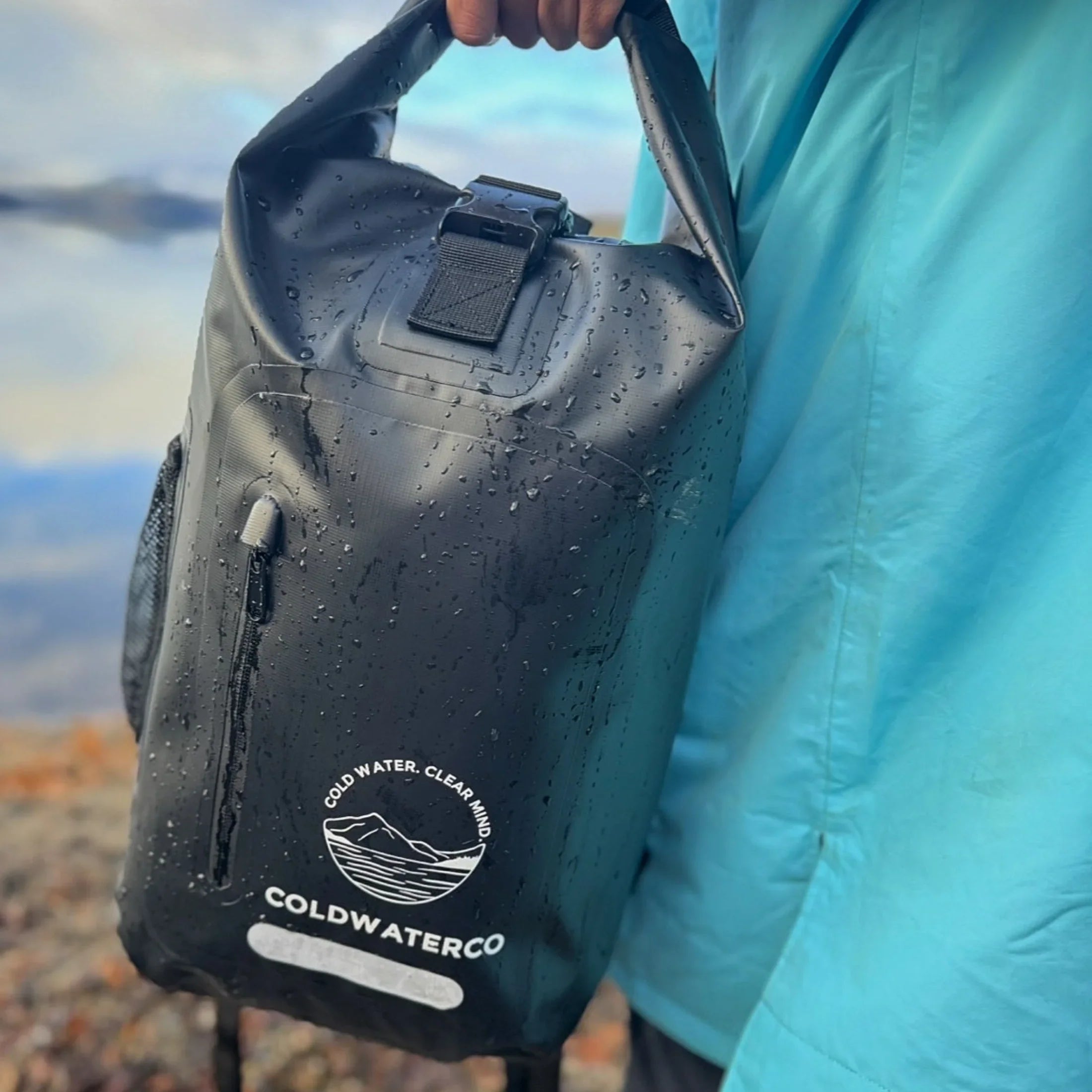 Black waterproof backpack shown in hand with water droplets on the bag.