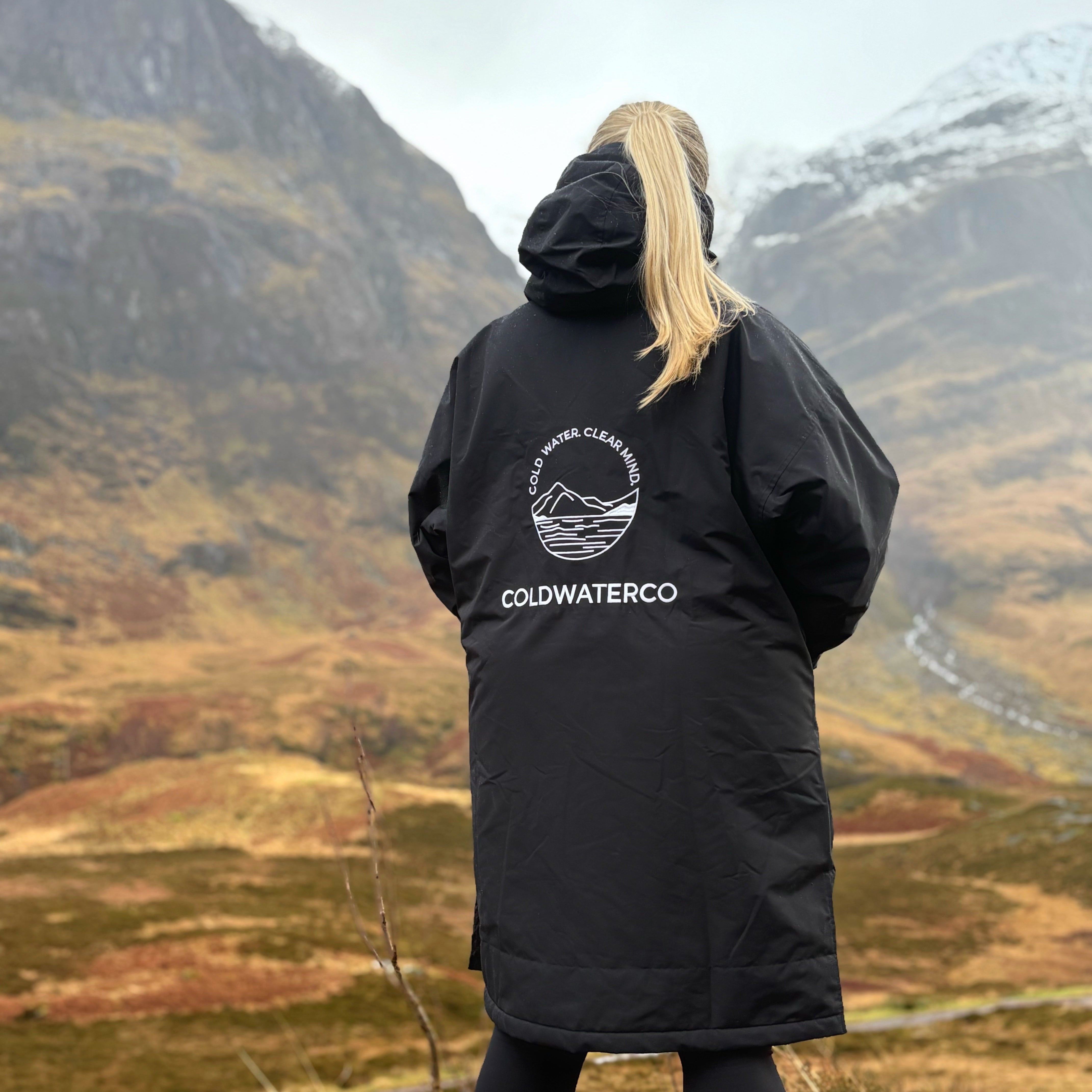Person wearing a black jacket with 'Coldwater Co' logo in a mountainous landscape