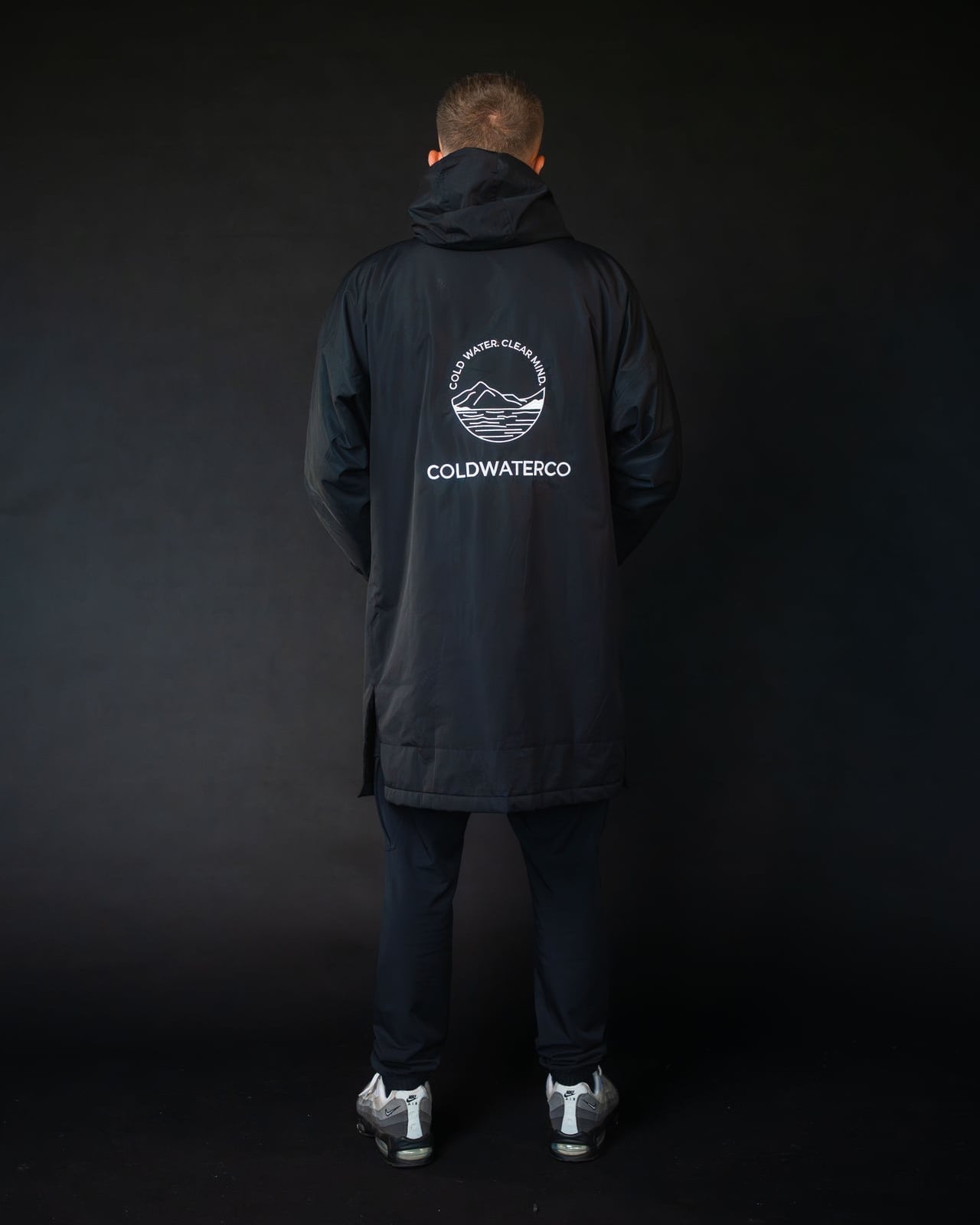 Person wearing a black coat with a visible brand logo on the back against a black background
