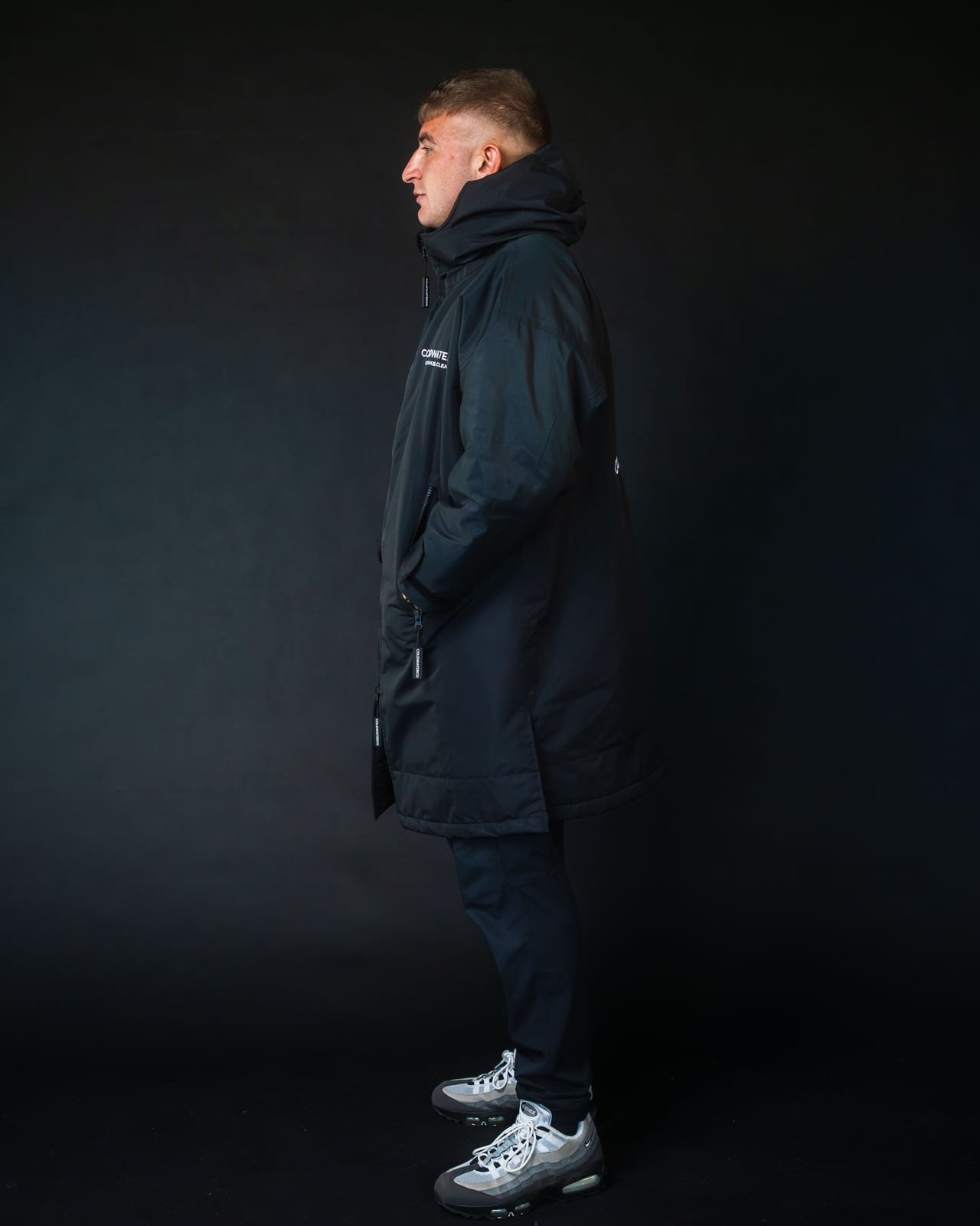 Person wearing a black coat standing against a dark background