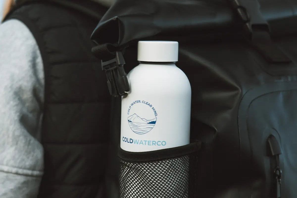 Person with a black backpack holding a white water bottle labeled 'Cold Water Co.' against a blue sky.