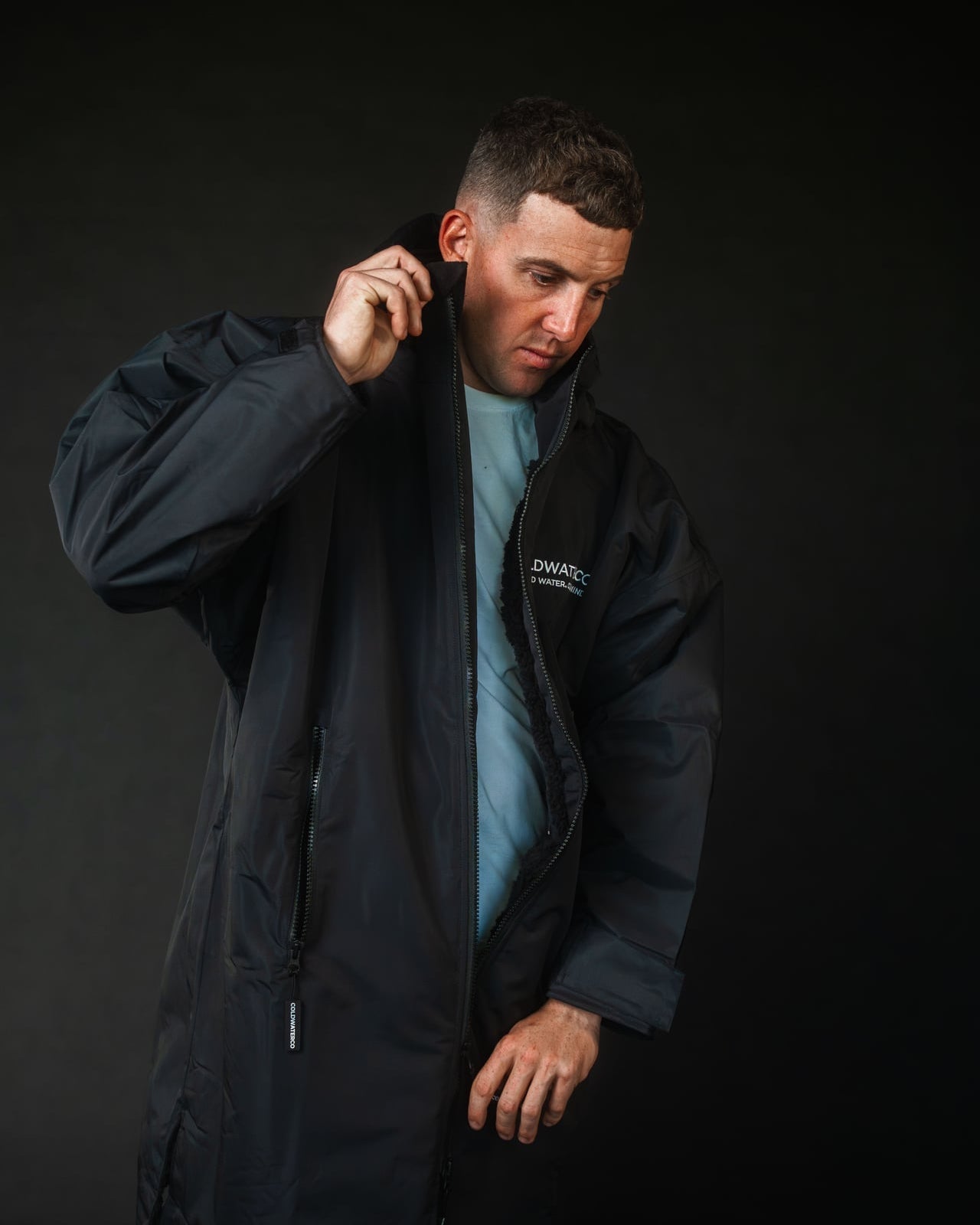 Man wearing a black jacket with a brand logo on a dark background
