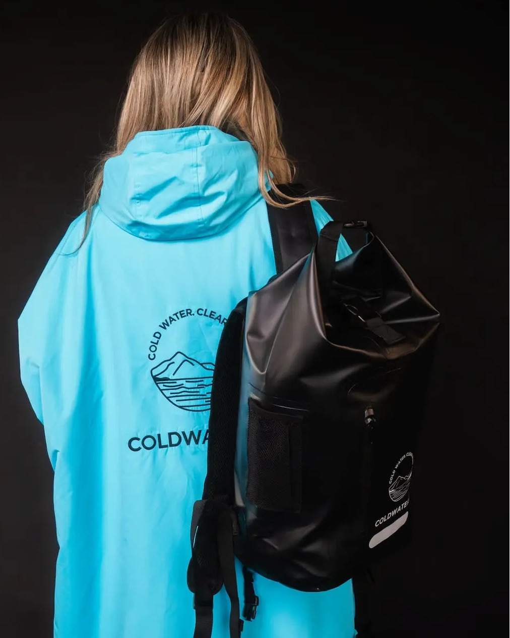 Person wearing a bright blue rain poncho with a black backpack on a dark background