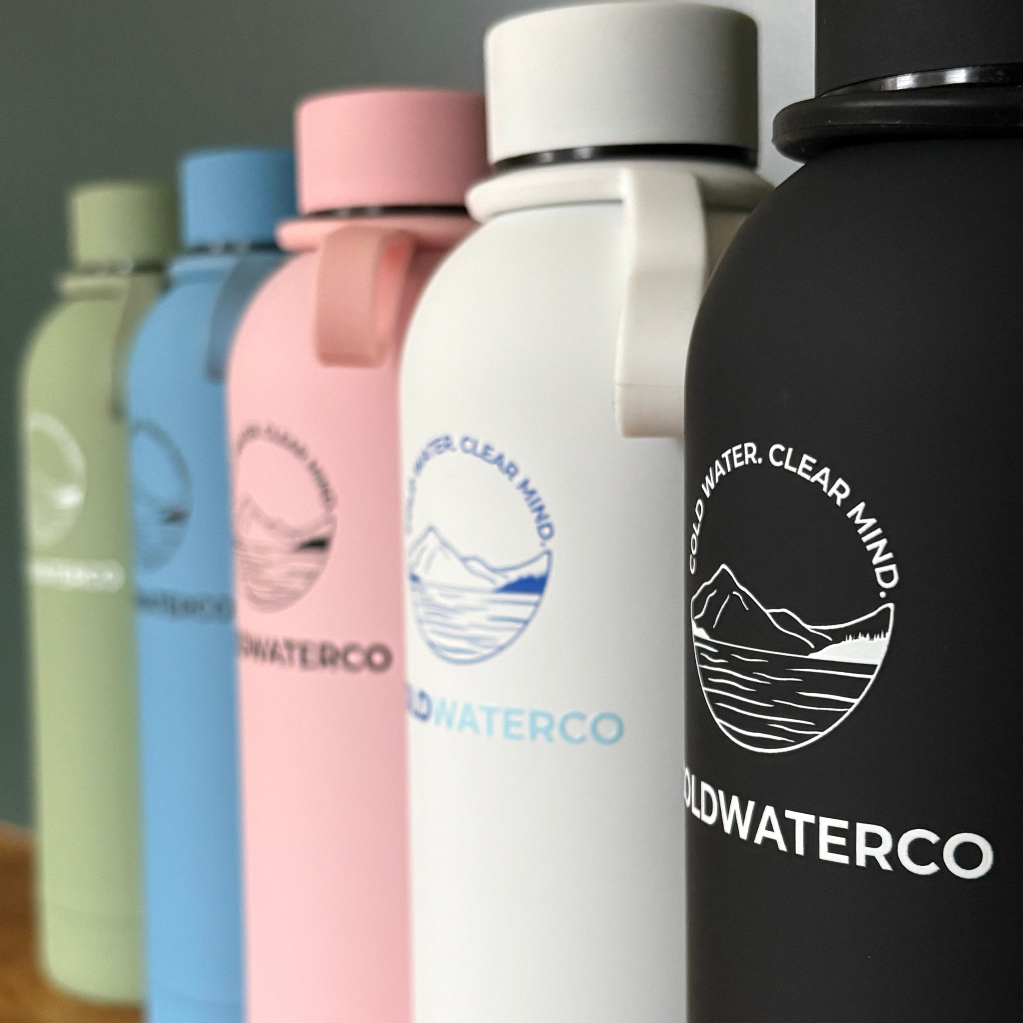 Stack of colourful bottles with 'Coldwaterco' branding on a reflective surface.