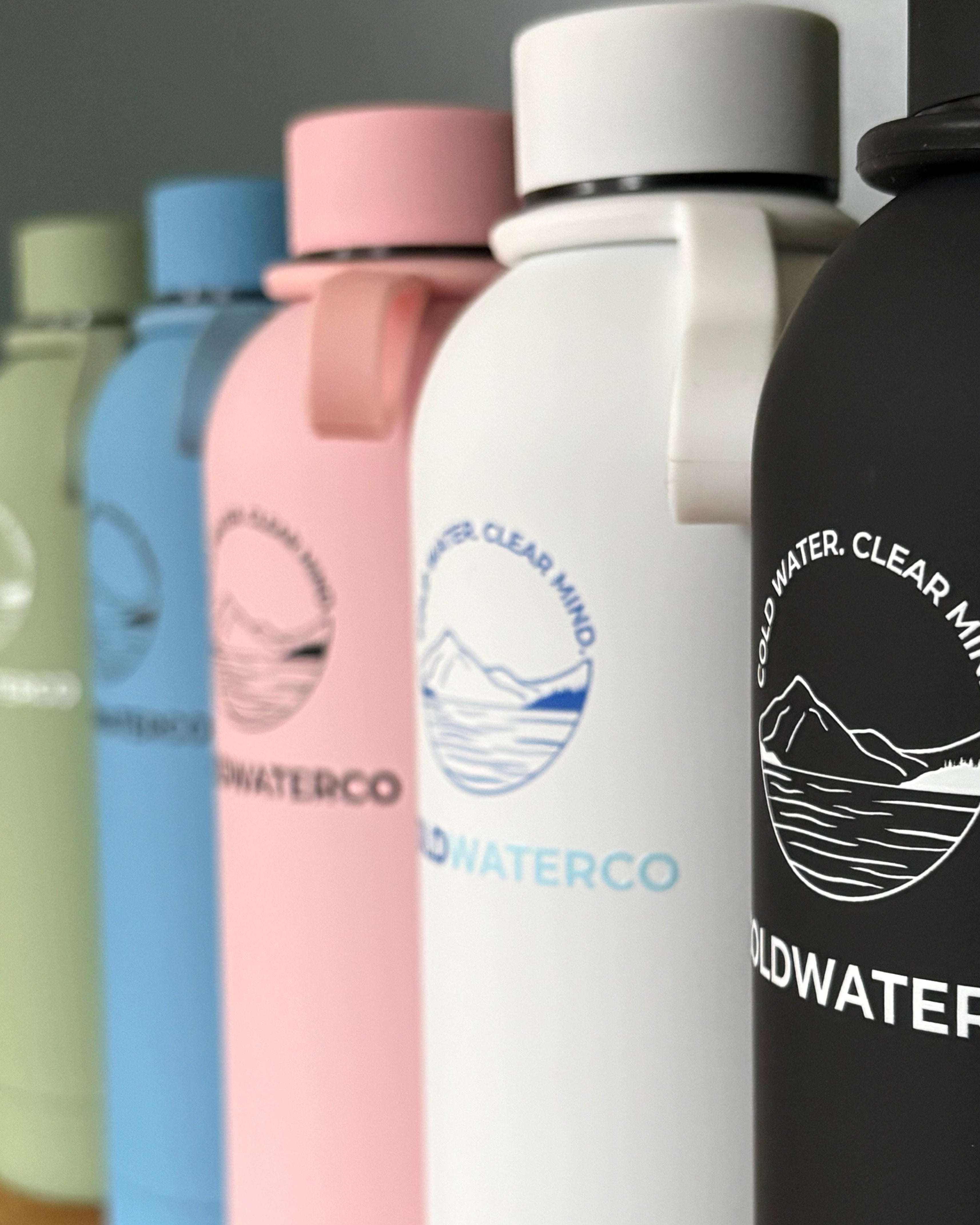 Stack of colourful bottles with 'Coldwaterco' branding on a reflective surface.