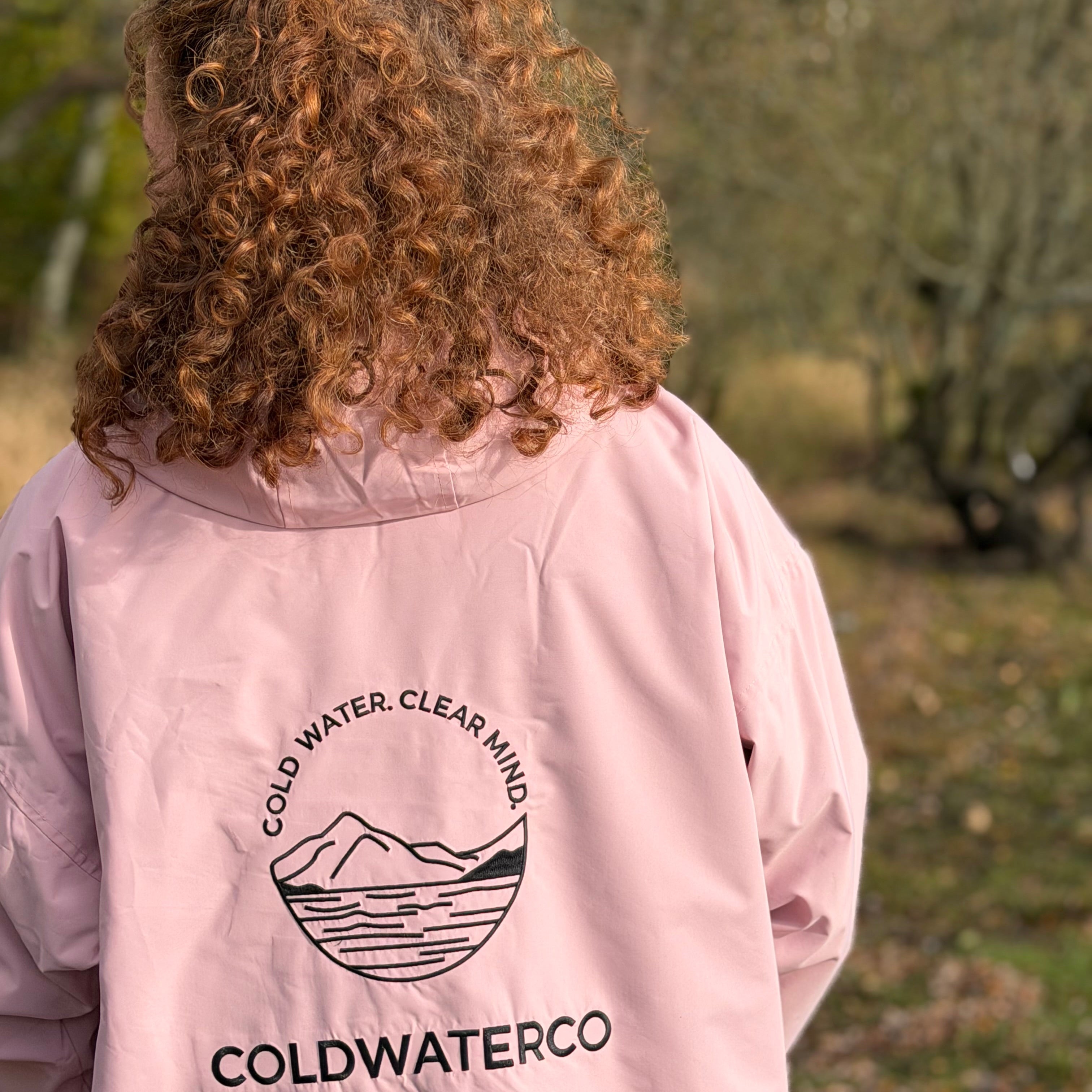 Person wearing a pink jacket with 'Coldwaterco' logo outdoors