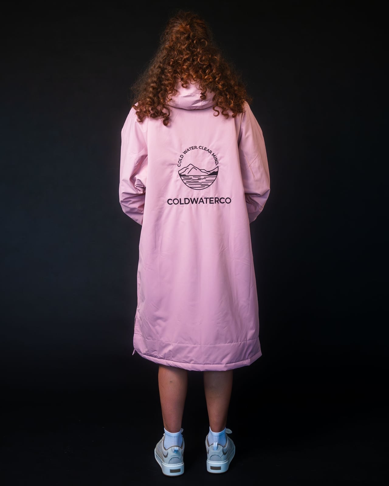 Person wearing a pink jacket with a logo on the back against a black background