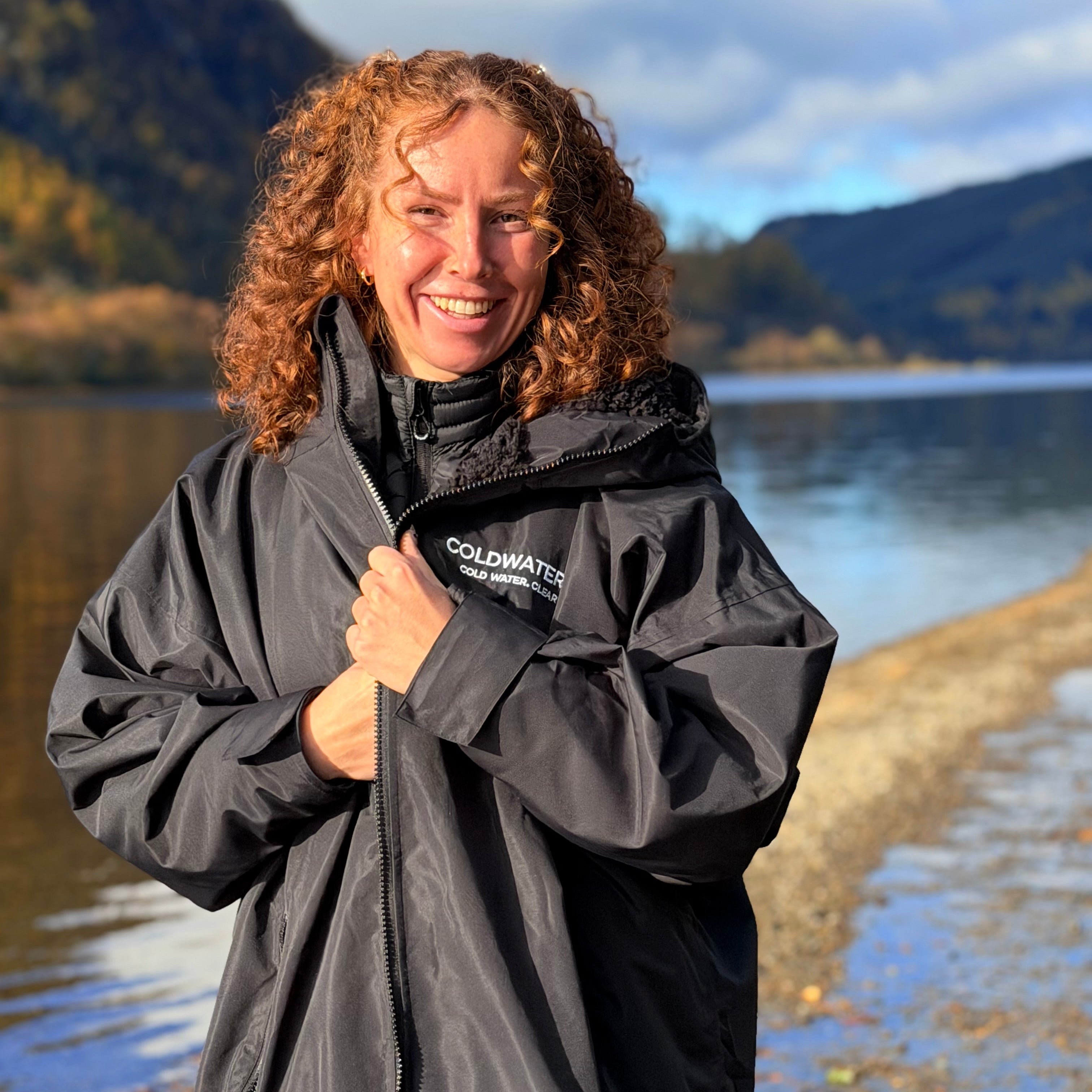 Person wearing a black Coldwater Co raincoat by a lake