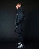 Person wearing a black coat standing against a dark background