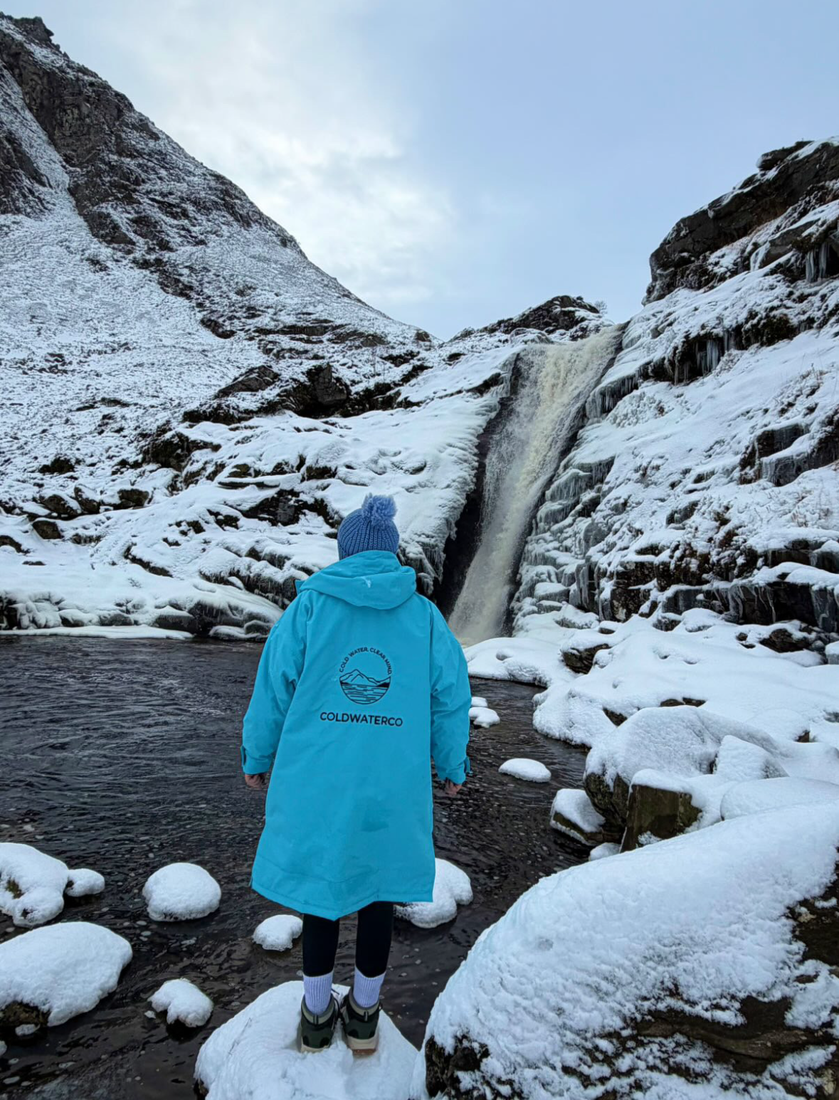 Woman wearing blue changing robe by snowy waterfall