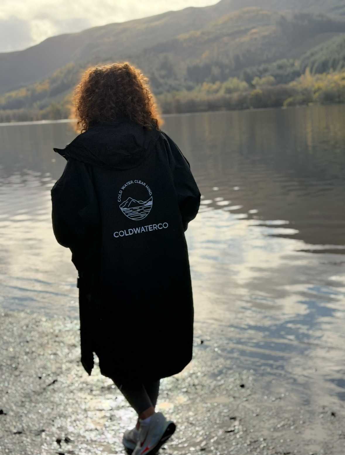 Women wearing a black ColdWaterCo changing robe walking along a loch
