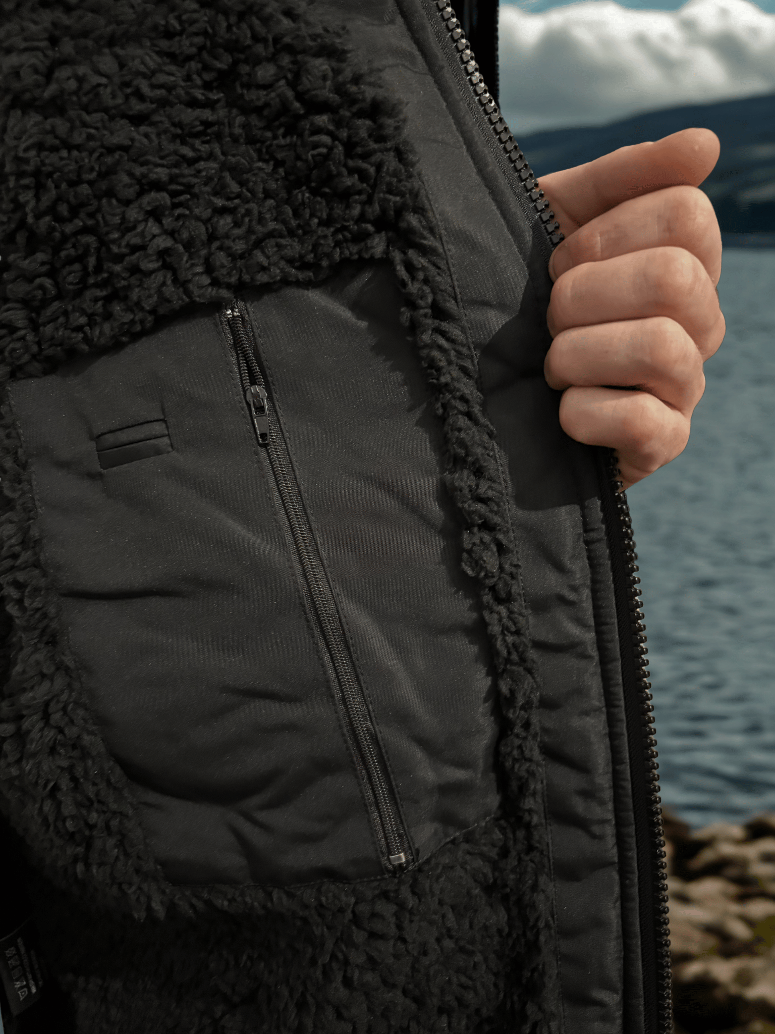 Close-up of a person wearing a black changing robe with a textured inner lining, holding onto a zipper, with a blurred natural background.