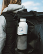 Person with a black backpack holding a white water bottle labeled 'Cold Water Co.' against a blue sky.