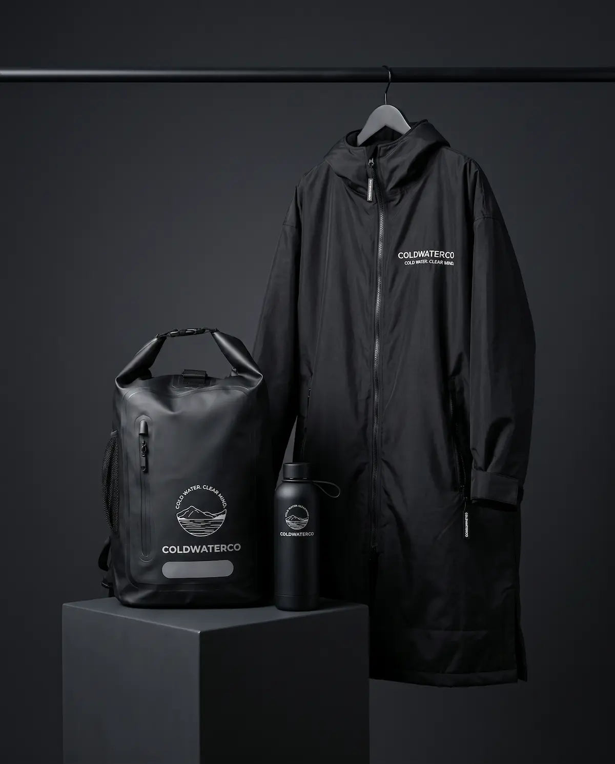 Black raincoat, backpack, and water bottle with 'Coldwater Co.' branding on a dark background.