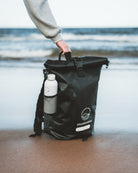 Black roll-top bag with a bottle on a beach