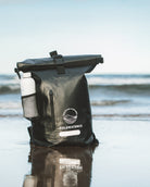 Black dry bag with a visible brand logo on a beach