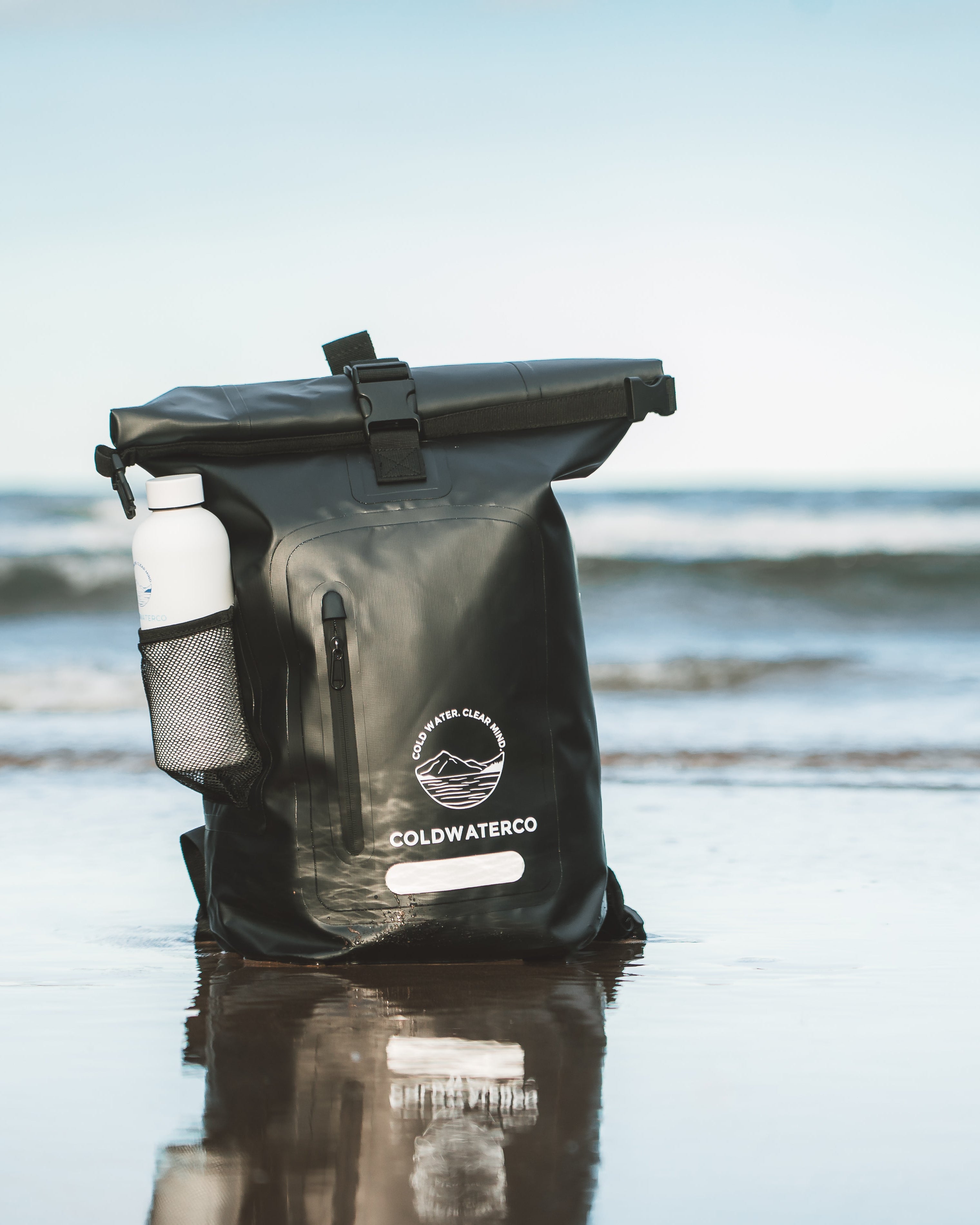 Black dry bag with a visible brand logo on a beach