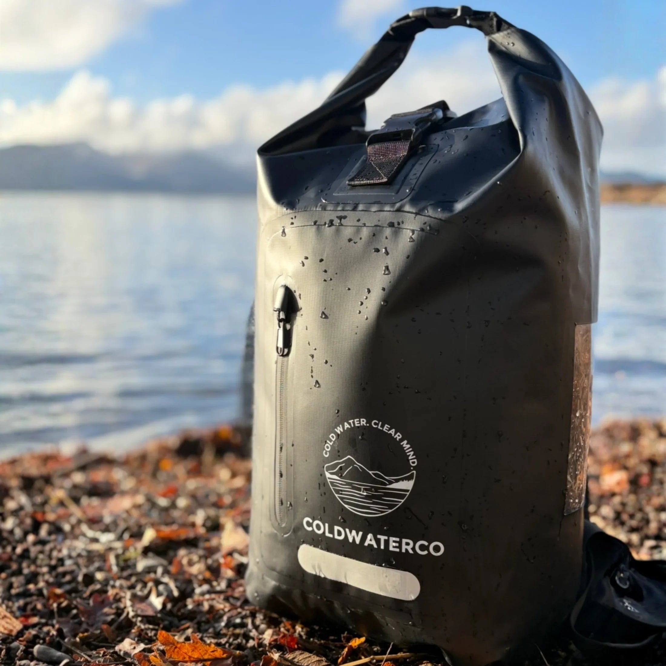 Black waterproof bag with 'Coldwater Co' logo on a beach