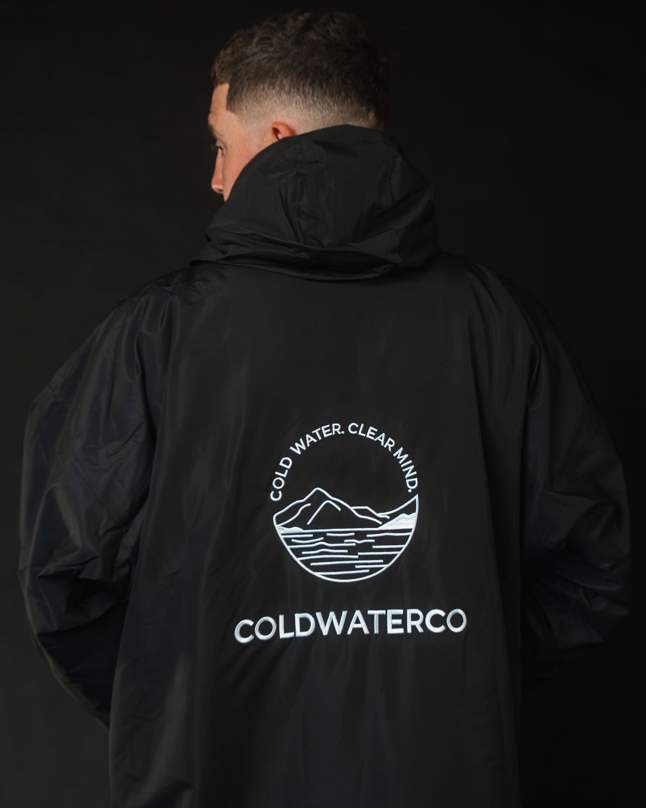 Person wearing a black jacket with ColdwaterCo logo on the back against a dark background