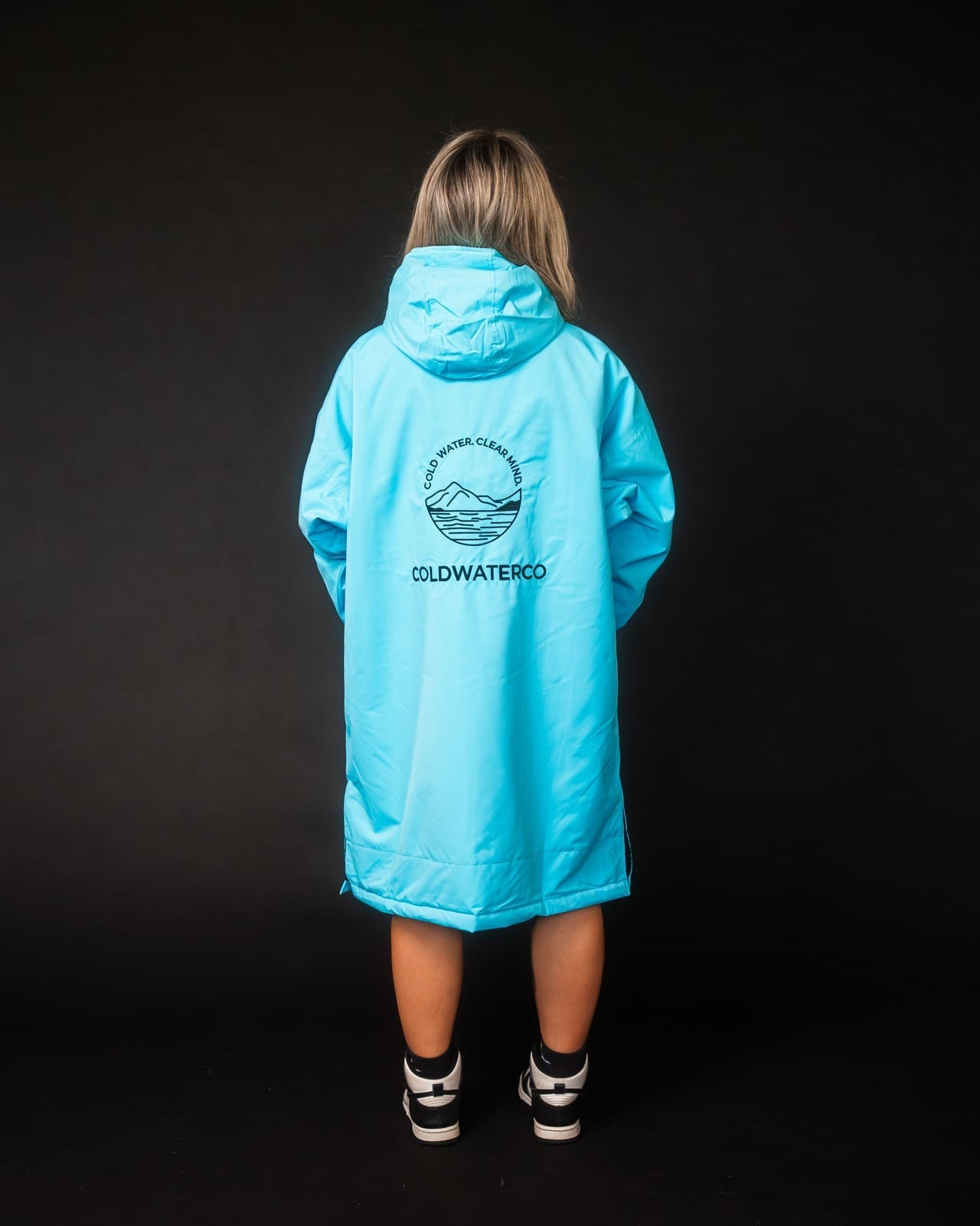 Person wearing a bright blue raincoat with a visible brand logo on the back against a black background