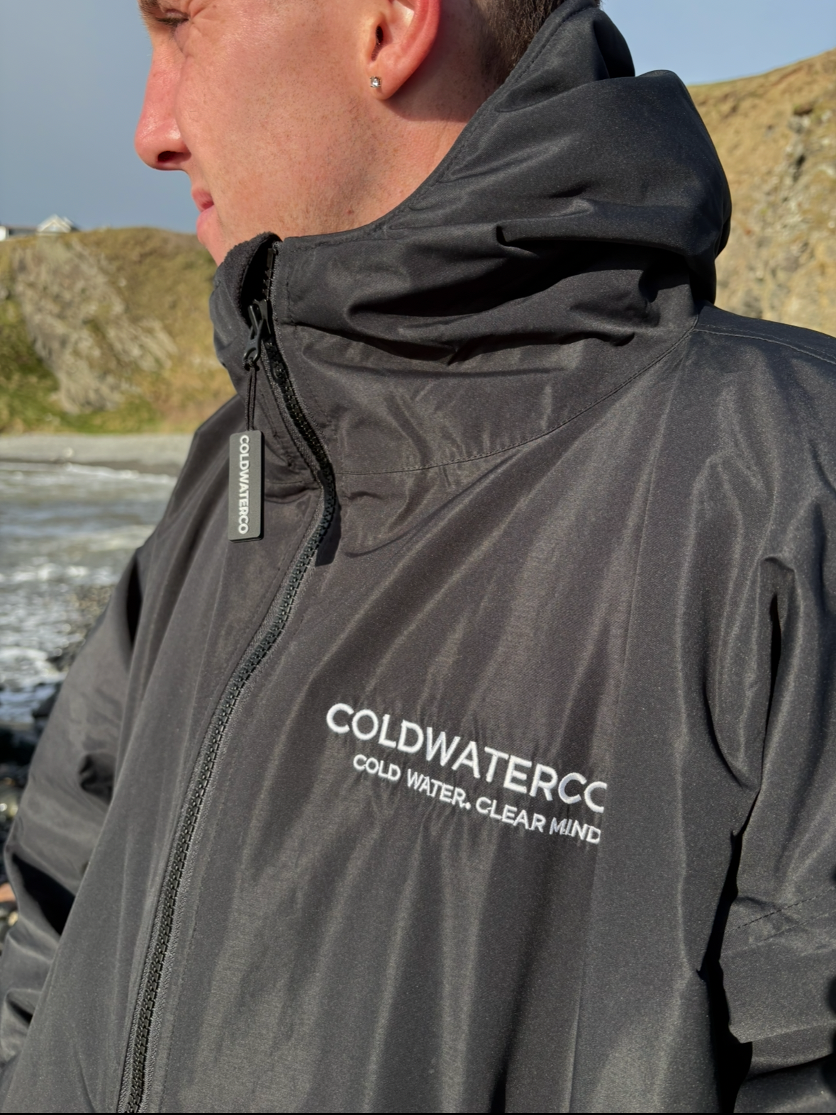Person wearing a black changing robe with 'COLDWATERCC' branding outdoors.