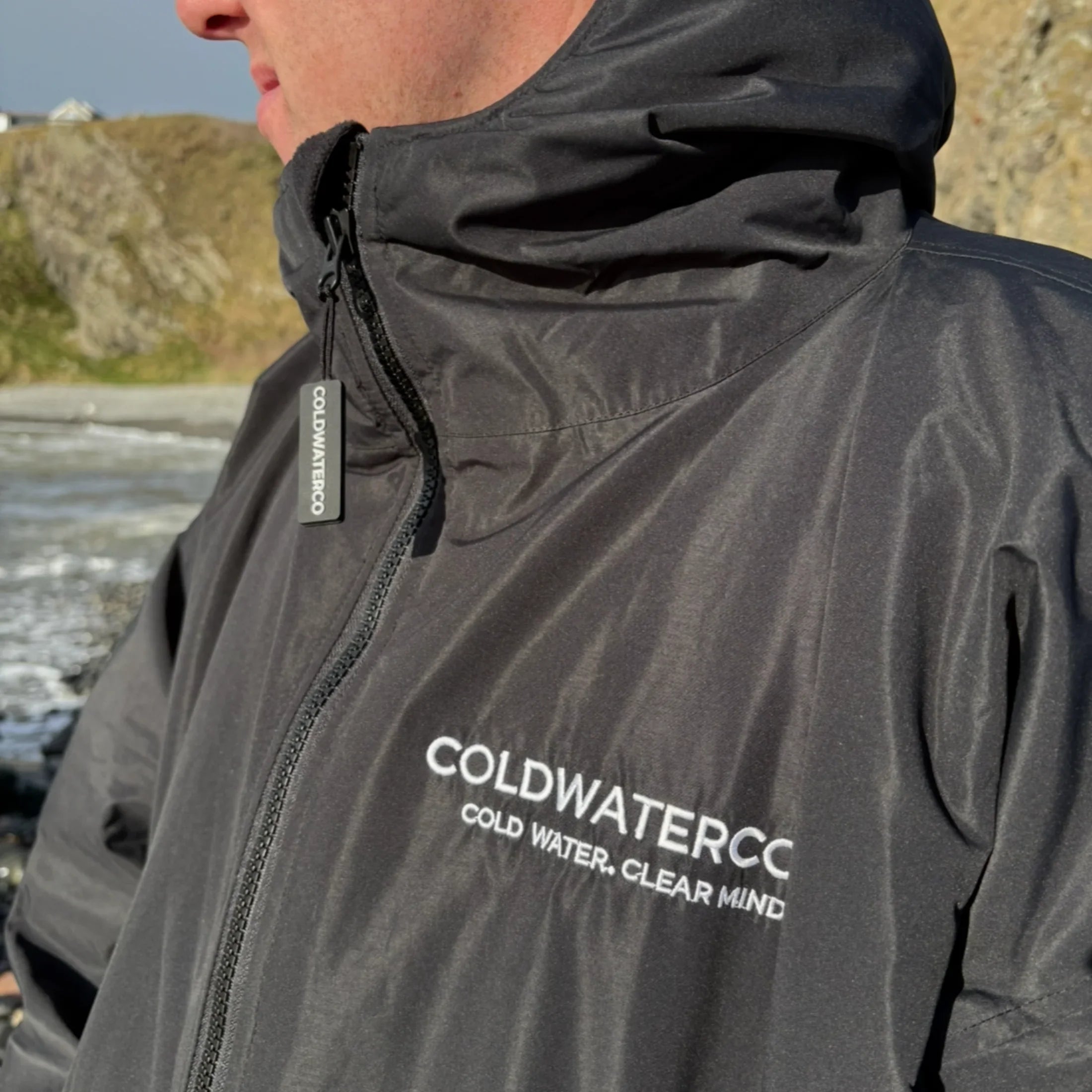 Person wearing a black changing robe with 'COLDWATERCC' branding outdoors.