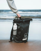 Black roll-top bag with a bottle on a beach