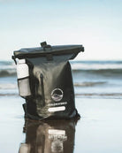 Black dry bag with a white label on a beach