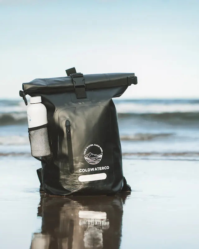 Black dry bag with a white label on a beach