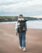 Person walking on a beach with a black backpack