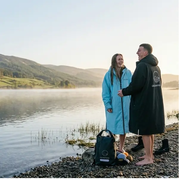 Two people standing by a lake, one wearing a blue coat and the other in a black coat with a ColdWaterCo brand logo.