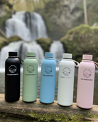 Five colorful water bottles on a log with a waterfall in the background