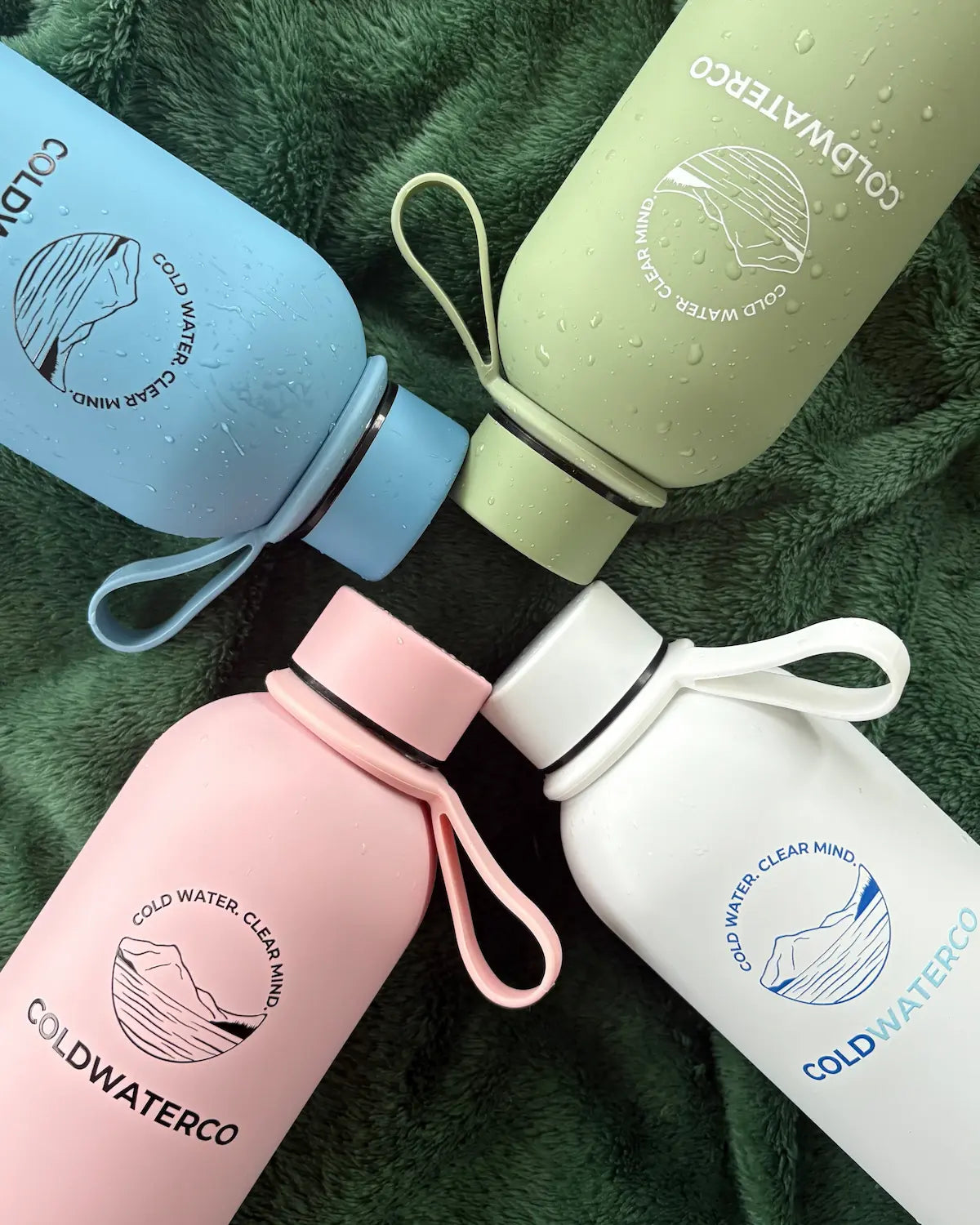Four colorful water bottles with 'COLDWATERCO' branding on a green textured background.