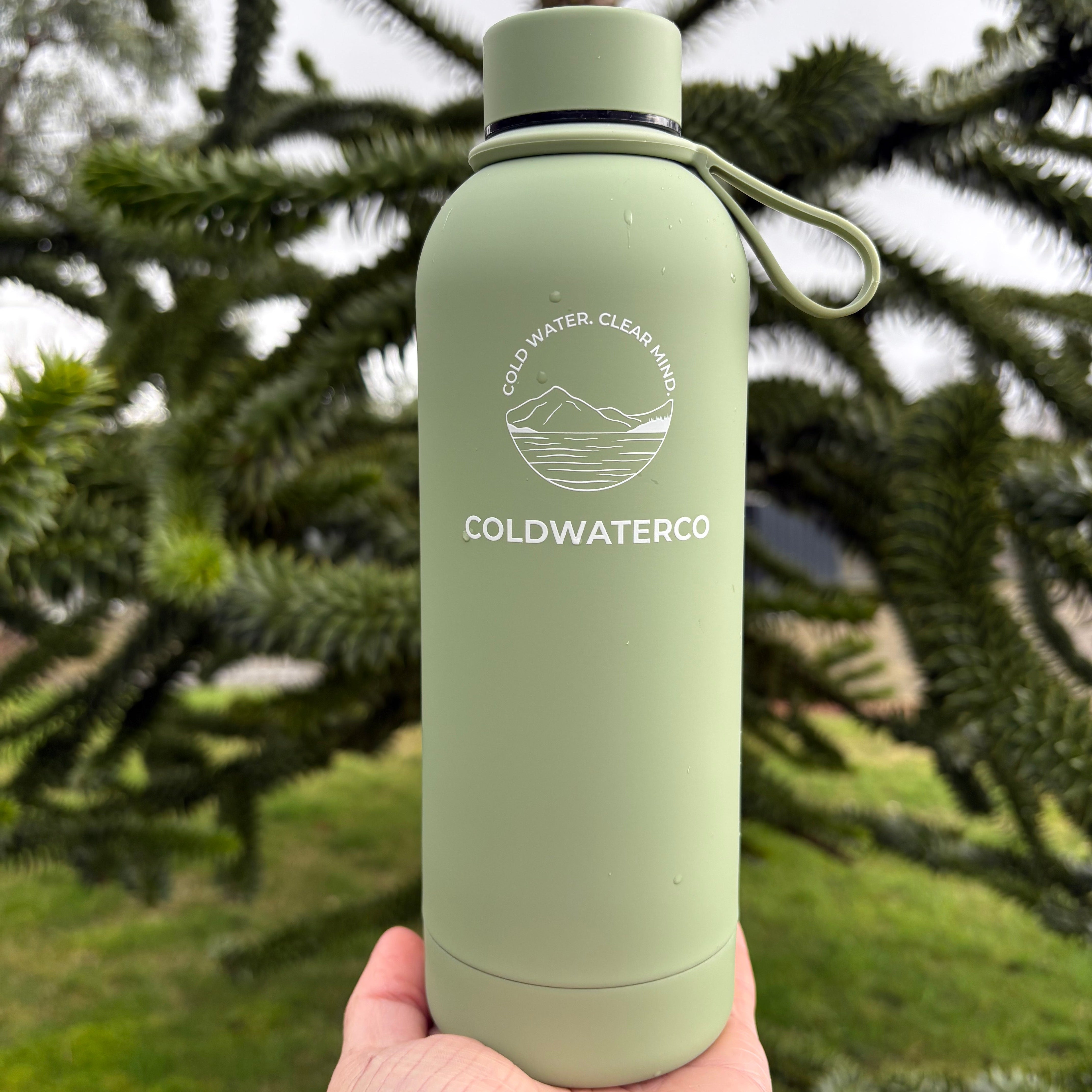 Green water bottle with 'COLDWATERCO' branding held by a hand against a natural background.