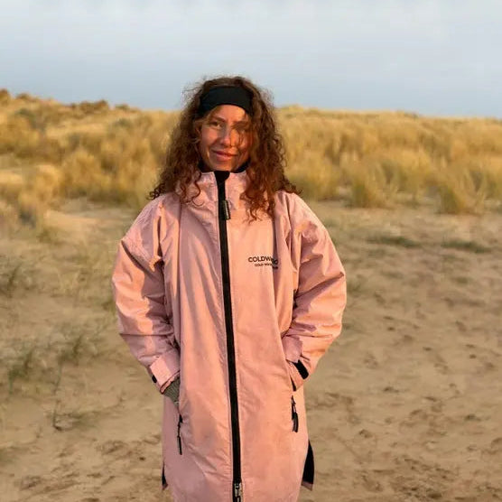 Person wearing a pink ColdWaterCo changing robe on a sandy dune