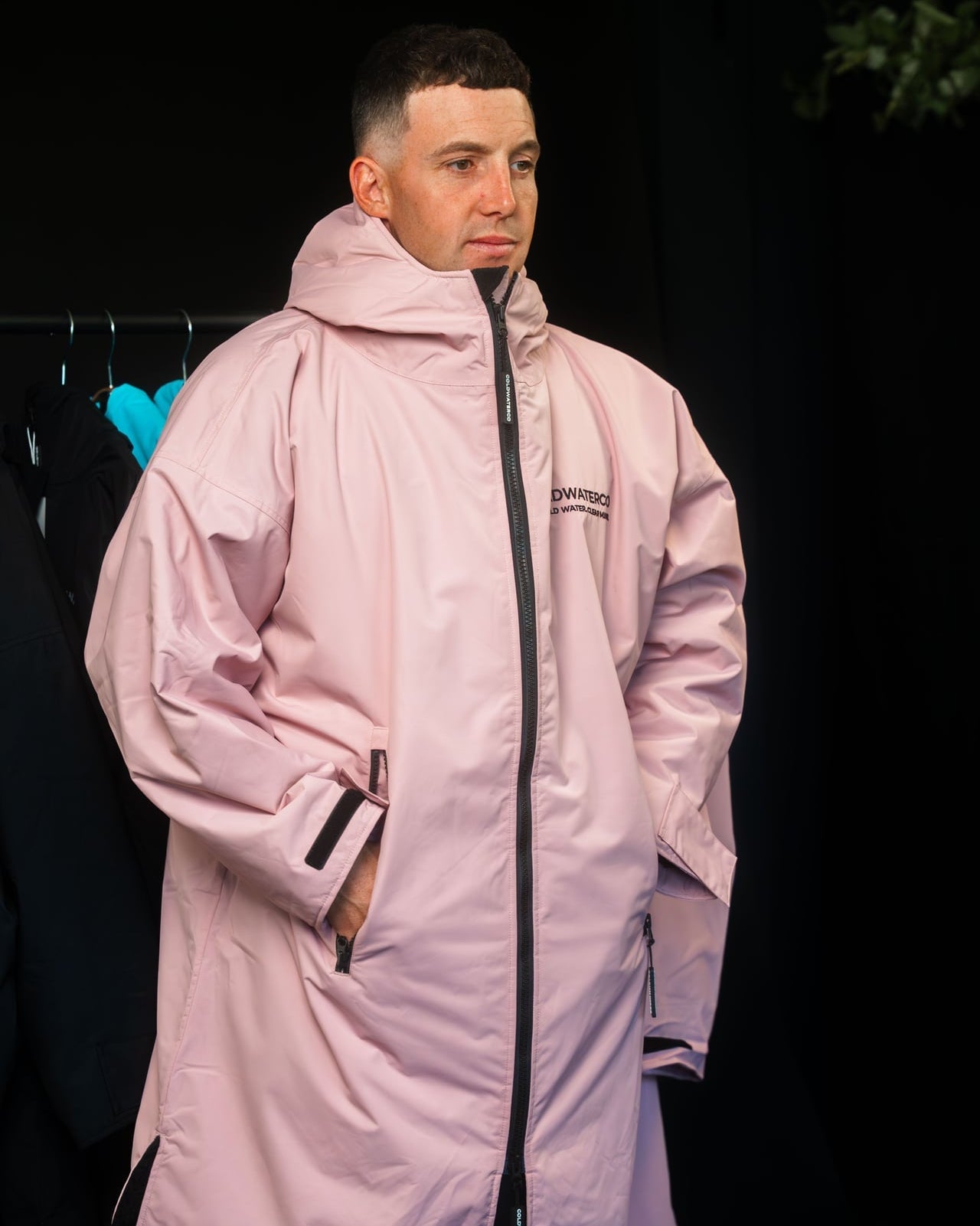 Person wearing a long pink coat with a brand logo on a black background