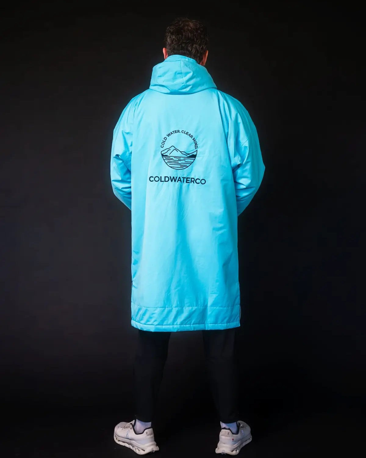 Man in blue ColdWaterCo changing robe with dark background