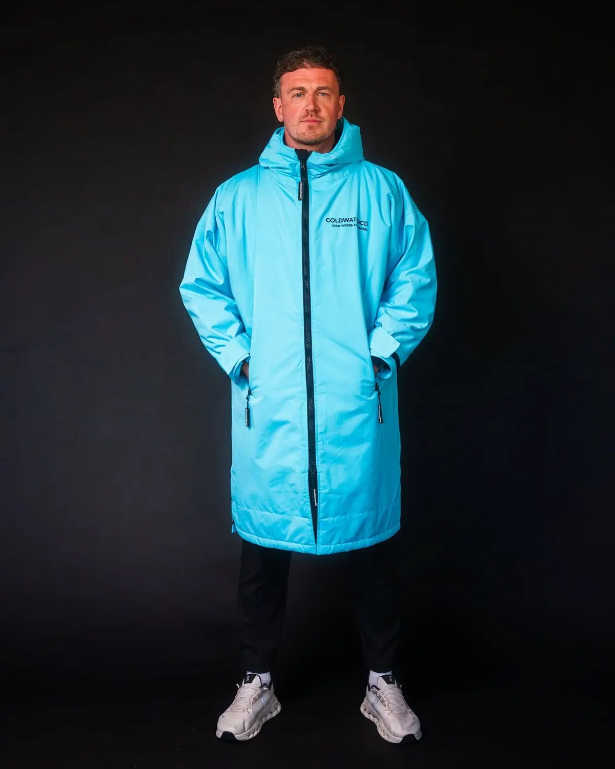Man in blue ColdWaterCo changing robe with dark background