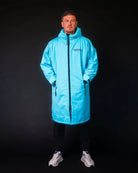 Man in blue ColdWaterCo changing robe with dark background