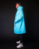 Man in blue ColdWaterCo changing robe with dark background