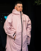 Man in pink ColdWaterCo changing robe with dark background