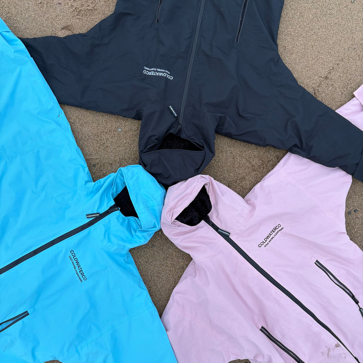 Three jackets in blue, black, and pink laid out on a textured surface.