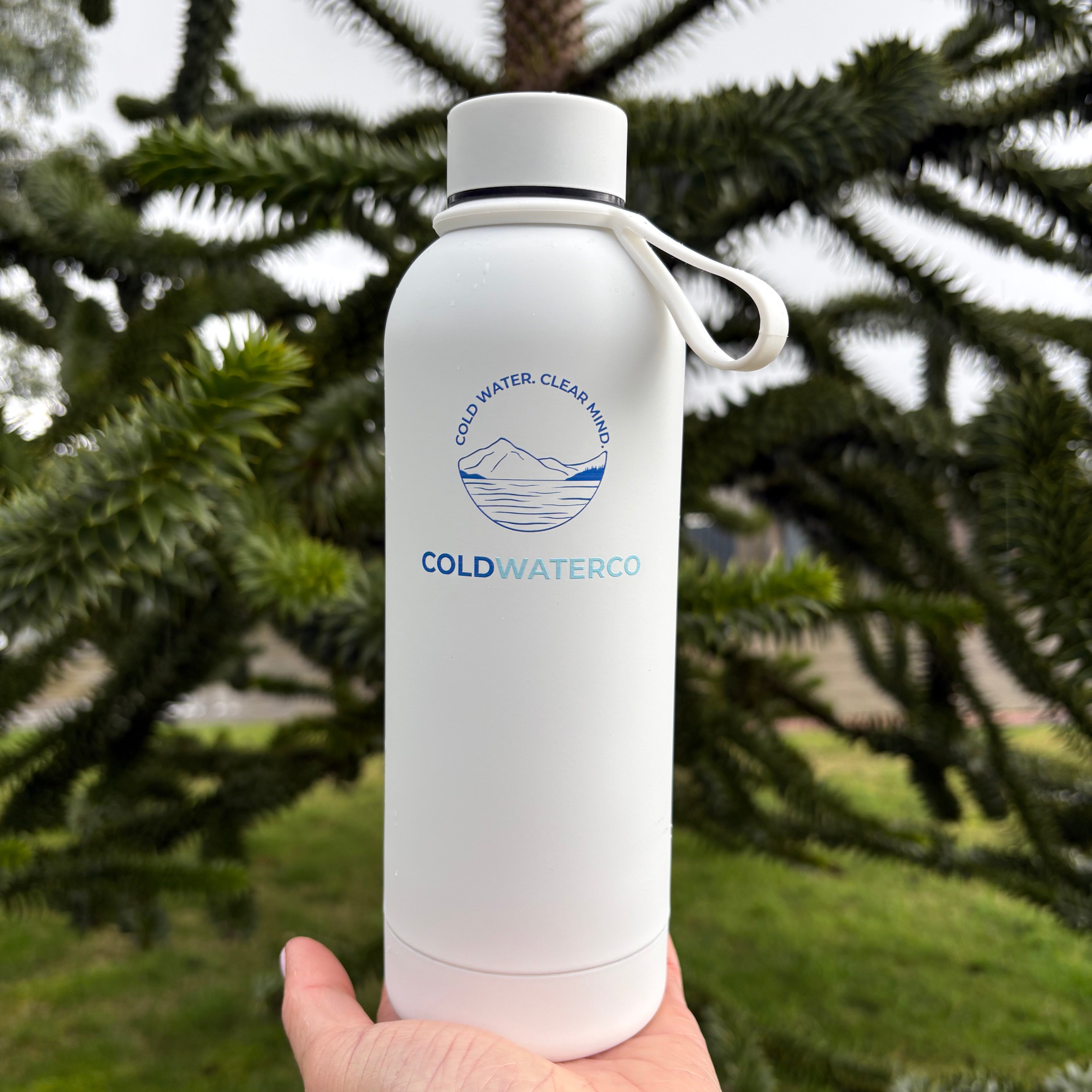 Hand holding a white water bottle with a brand logo against a green leafy background
