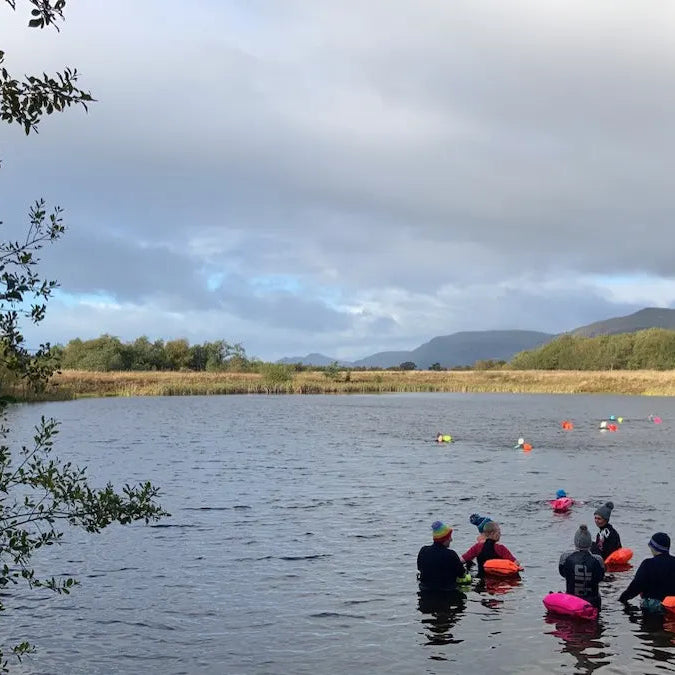 People with colourful floats on a lake with trees and mountains in the background