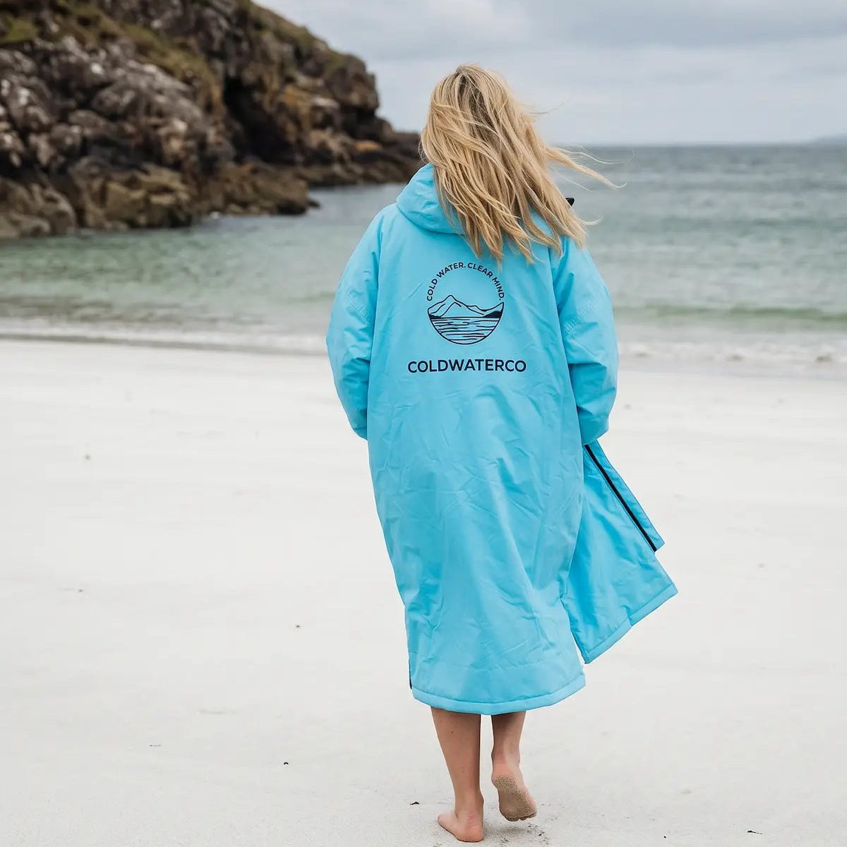 Woman walking on white beach with Arctic Blue Cold water co Changing robe